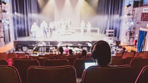 Person sitting in the stalls of the Mumford Theatre while students rehearse on stage
