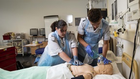 Two nursing students working with a medical mannekin on a mock hospital ward