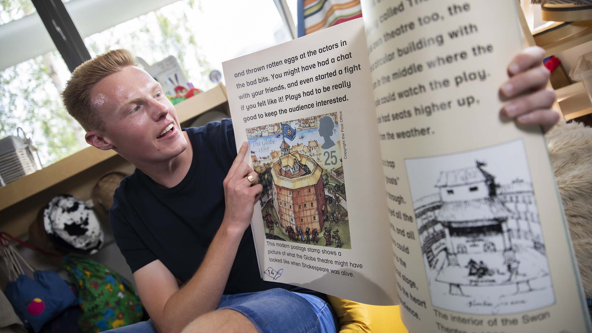 Education student in a mock classroom holding up a children's book and reading it aloud