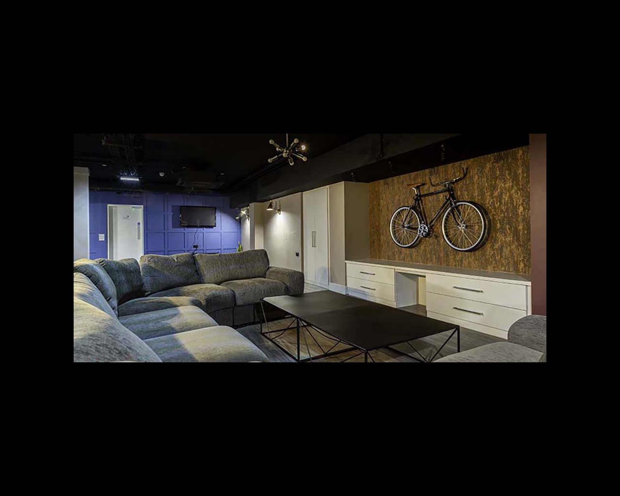 Sofas around a low table, with a bike hanging on the wall and a TV in the distance, in Cambridge's CB1 accommodation