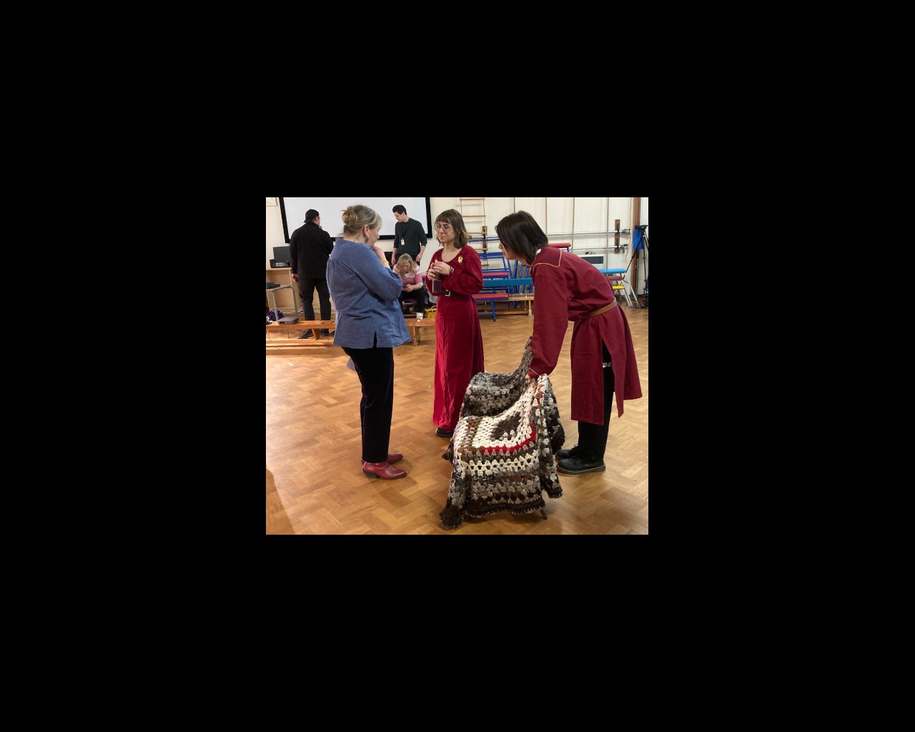 Two drama students dressed in red chinese-style costumes talking to lecturer