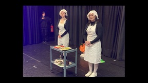 Two female drama students dressed in old-fashioned nurse uniforms with trolley of food on stage