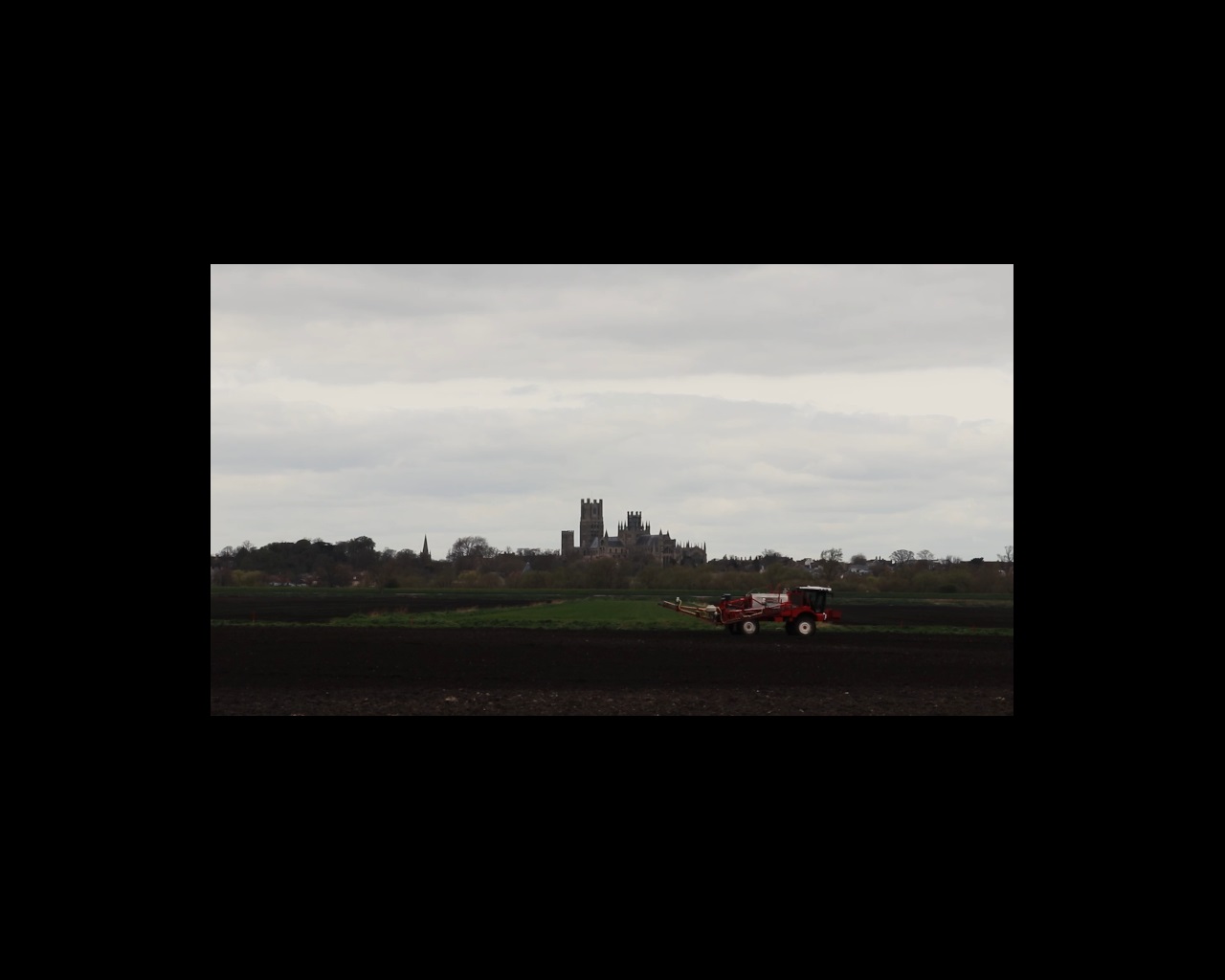 Film still of combine harvester in field with Ely Cathedral in distance
