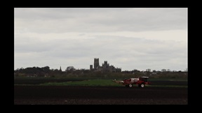 Film still of combine harvester in field with Ely Cathedral in distance